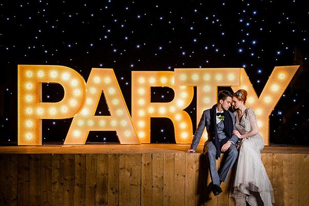 A man and woman sitting next to illuminated letters that spell party
